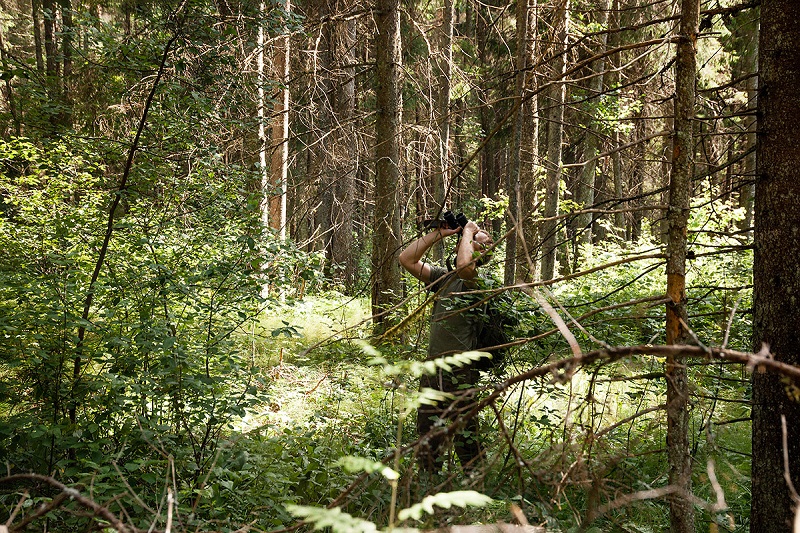 Man with boniculars in the forest. 